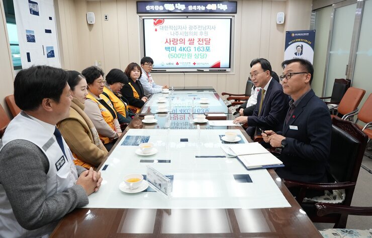 회의실에서 나주시 관계자들(나주시장 윤병태 포함)과 대한적십자사 봉사자들이 테이블에 둘러앉아 '대한적십자사 광주전남지사 - 나주시협의회 후원 사랑의 쌀 전달 백미 4KG 163포(500만원 상당)' 현수막이 걸린 스크린 앞에서 회의하고 있는 전경