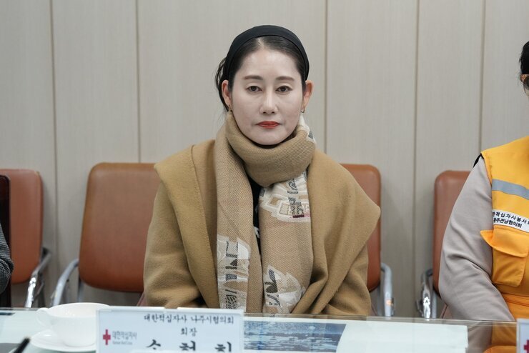 카멜색 스카프를 두른 여성이 정면을 응시하며 회의 테이블에 앉아 있는 클로즈업 사진