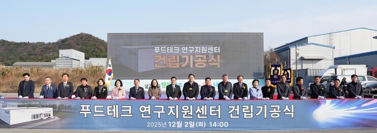 푸드테크 연구지원센터 건립기공식 커팅식 단체 사진. 야외 행사장 무대 아래에서 약 20여 명의 주요 참석자들이 커팅용 흰색 장갑을 끼고 기념 리본을 자르기 위해 서 있다. 배경 스크린에는 '푸드테크 연구지원센터 건립기공식 2025년 12월 2일 (화) 14:00' 문구가 보인다.