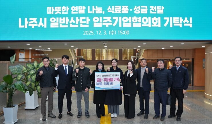  나주시 일반산단 입주기업협의회 기탁식 단체 사진. '따뜻한 연말 나눔, 식품품·성금 전달'이라는 현수막 아래, 나주시 관계자들과 기업협의회 회원들로 보이는 9명이 성금/후원물품 기탁 내용이 적힌 패널을 들고 주먹을 쥐고 기념 촬영을 하고 있다.