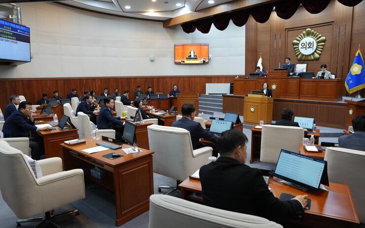  시의회 본회의장 전경. 의원들이 책상에 앉아 있고, 중앙 단상에서 발언하는 사람이 있으며, 벽면 스크린에는 '의회' 글자와 회의 내용이 보임