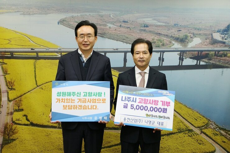 왼쪽에 시장님이 성원해주신  고향사랑! 가치있는 기금사업으로 보답하겠습니다. 라고 적힌 팻말을 들고 오른쪽에 나주시 고향사랑 기부 금 5,000,000원 용천산업(주) 나명균 대표라고 적힌 팻말을 들고 기념 촬영 중이다