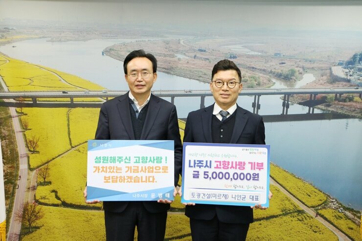 왼쪽에 시장님이 성원해주신  고향사랑! 가치있는 기금사업으로 보답하겠습니다. 라고 적힌 팻말을 들고 오른쪽에 나주시 고향사랑 기부 금 5,000,000원 토광건설(미르채) 나안균 대표라고 적힌 팻말을 들고 기념 촬영 중이다