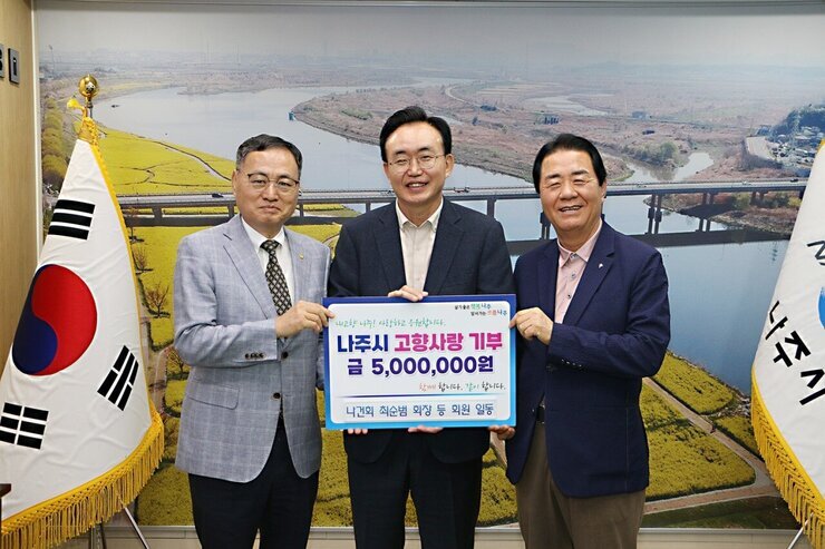  살기좋은 행복 나주 앞서가는 으뜸 나주 내고향 나주! 사랑하고 응원합니다. 나주시 고향사랑 기부 금 5,000,000원 함께 합니다. 같이 합니다. 나건회 최순범 회장 등 회원 일동이라고 적힌 팻말을 들고 있는 윤병태 시장과 중년 남성 2명