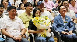 파리올림픽 금메달리스트 안세영 선수 나주 환영행사 안세영 선수가 꽃다발을 들고 자리에 앉아 수줍게 환영 축하 영상을 바라보고 있는 모습 