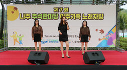 추석맞이 다문화가족 노래자랑 이주여성 3명이 무대 위에 올라 한명은 마이크를 잡고 노래를 부르고 있으며 2명은 춤을 추기 위해 준비를 하고 있는 모습