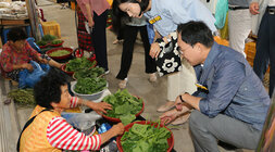 추석 명절맞이 나주목사고을시장 장보기 행사 나주시장과 배우자가 목사고을시장 한켠에 앉아 호박잎을 판매하고 있는 여성 어르신과 함께 앉아서 이야기를 나누고 있는 모습