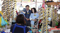추석 명절맞이 나주목사고을시장 장보기 행사 나주시장과 배우자가 어물전에서 생선을 구매할려고 서 있는 모습 사진 좌우 양 옆으로 조기가 꼬아져서 걸려있는 모습이 보이고 여성 상인분의 뒷모습도 보인다