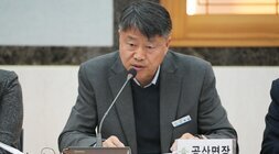 회의에 참석한 중년 남성이 '공산면장' 명패를 앞에 두고 마이크를 잡고 발언하는 모습. 짙은 회색 재킷을 입고 있다.