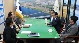 다섯 명의 남성(나주시장 윤병태 포함)이 큰 녹색 테이블에 둘러앉아 회의를 하는 모습. 정장을 입은 사람들이 보이며, 테이블 위에는 서류와 찻잔이 놓여 있다. 뒤쪽 벽에는 태극기와 나주 로고가 있는 깃발, 그리고 강이 보이는 야외 전경 사진이 걸려 있다.