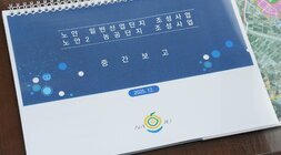 '노안 일반산업단지 조성사업 노안2 농공단지 조성사업 중간보고 2025. 12.' 날짜가 표시된 스프링 달력의 표지 클로즈업 사진. 표지 하단에는 나주시 로고가 있다.