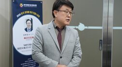 정장 차림의 한 남성이 서서 이야기 하는 모습