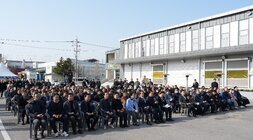 푸드테크 연구지원센터 건립공사 기공식 참석자 전경. 야외 공터에서 많은 참석자들이 일렬로 놓인 의자에 앉아 앞쪽 무대를 향해 경청하고 있다. 뒤쪽으로는 공장 또는 창고 건물들이 보인다.