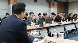 회의 또는 간담회 장면. 테이블에는 참석자들이 앉아 자료를 검토하거나 경청하고 있다.