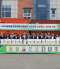 나주쌀 새청무 헝가리 첫 수출 상차식 조합법인 앞 마당에서 나주시장과 나주시의회의장, 각 단위농협 조합장 및 관계자들이 행사를 위해 새청무 쌀이 놓여진  긴 테이블 뒤에 서서 화이팅을 하며 기념촬영을 하고 있는 모습
