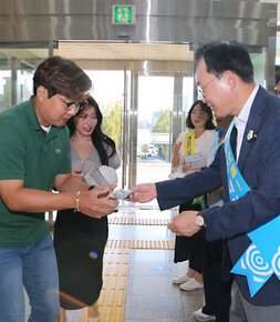 공무원 노조와 함께하는 추석맞이 청렴캠페인 나주시장이 청렴 관련 어깨띠를 메고 현관 로비에서 출근을 하고 있는 남성 직원에게 청렴캠페인 관련 물품을 나눠주고 있는 모습