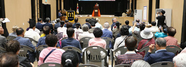 전국 시조창 나주 경연대회 무대 위의 여성 참가자가 자리에 서서 경연을 하고 있는 모습과 참석자들이 앉아서 듣고 있는 뒷모습