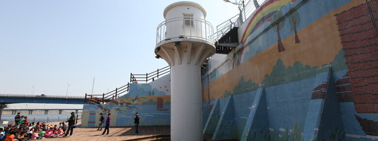 영산포 등대를 찍은 사진. 하얀 등대 옆으로 높은 벽이 있으며 그 앞으로 여러사람들이 앉아 있음.